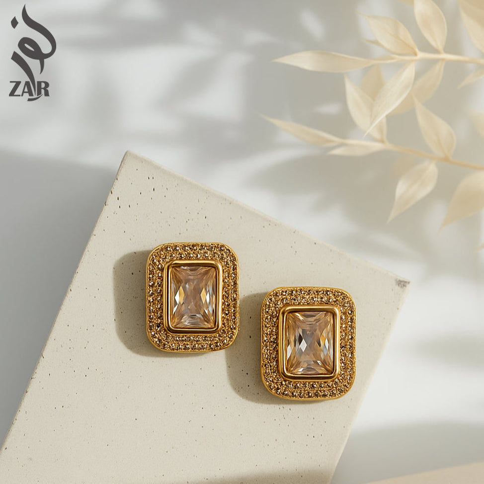 Gold earrings with gemstones on a light surface, featuring the ZAR brand.