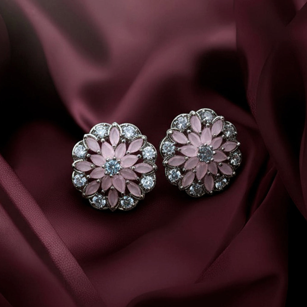 Pair of floral earrings with pink center and silver accents on a maroon fabric background.