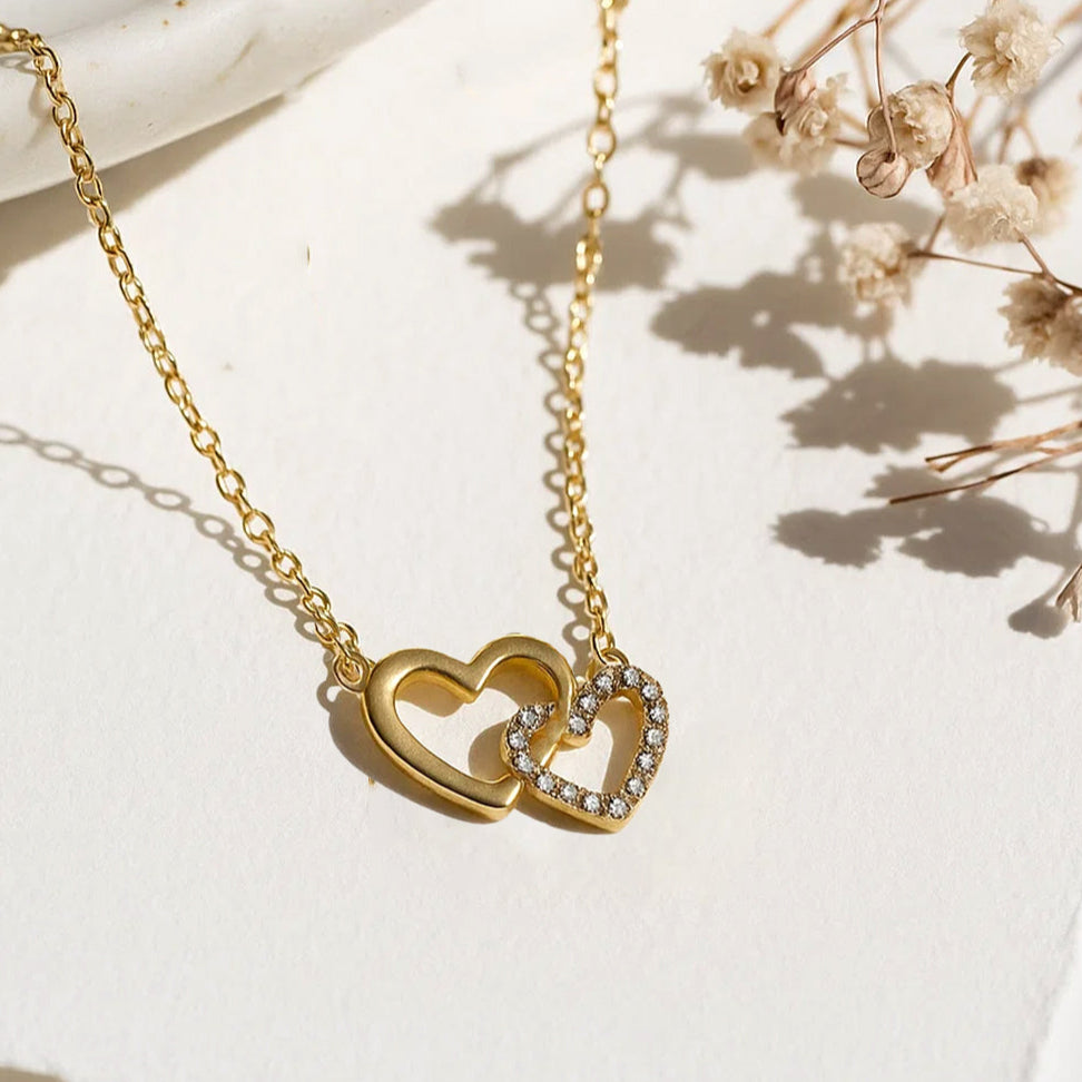 Gold necklace with interlocking heart pendants on a light background with dried flowers.