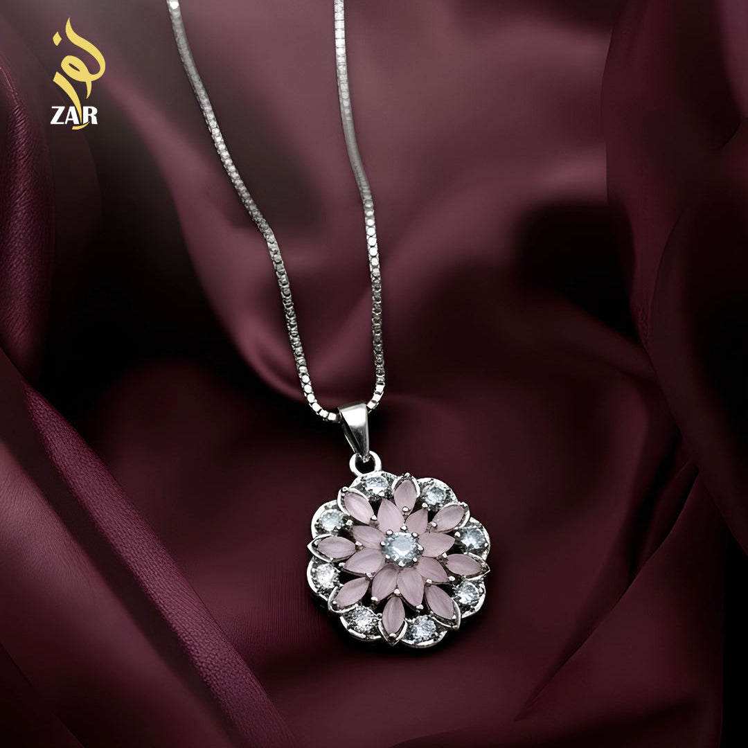 Silver necklace with a pink floral pendant on a dark fabric background
