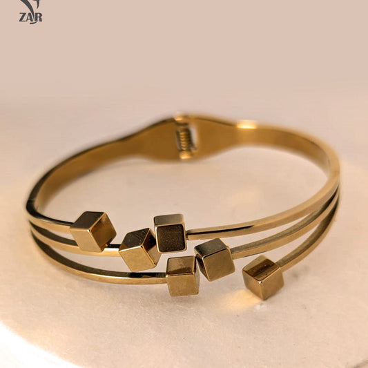 Gold bracelet with geometric cube designs on a beige background