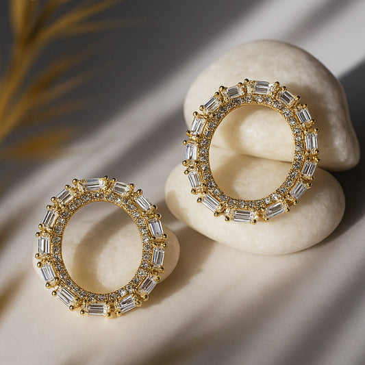 Gold hoop earrings with clear gemstones on a stone surface