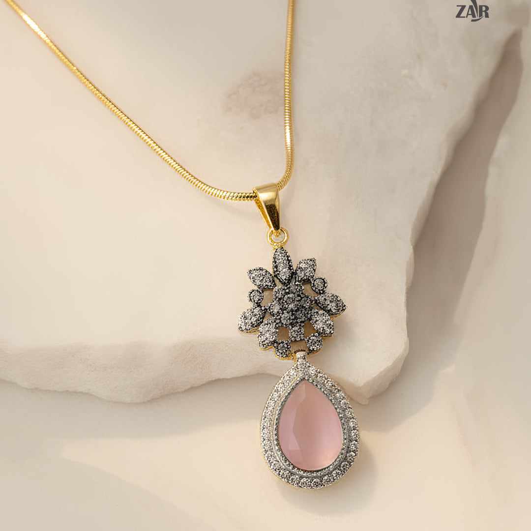 Gold necklace with a pink teardrop pendant on a beige background, featuring the ZAR brand.