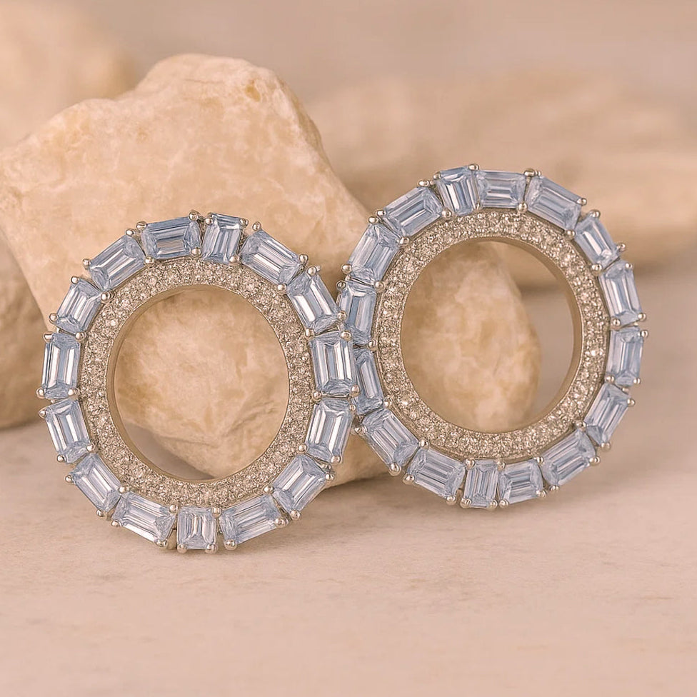 Elegant earrings with gemstones on a beige stone background, featuring the ZAR brand.